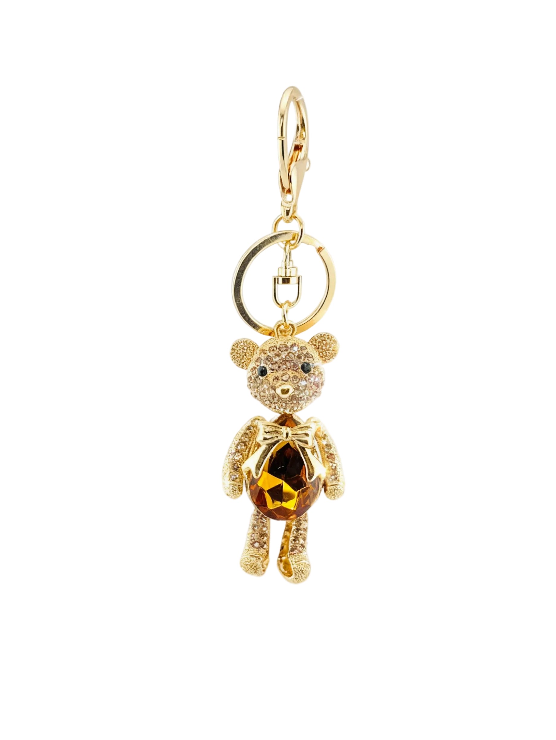 A gold-tone teddy bear keychain charm embellished with clear rhinestones and featuring a faceted amber-brown gemstone in its belly, attached to a split key ring on a white background.